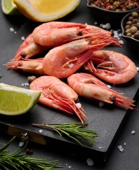 Boiled shrimp on a board, lemon slices, spices on a black background