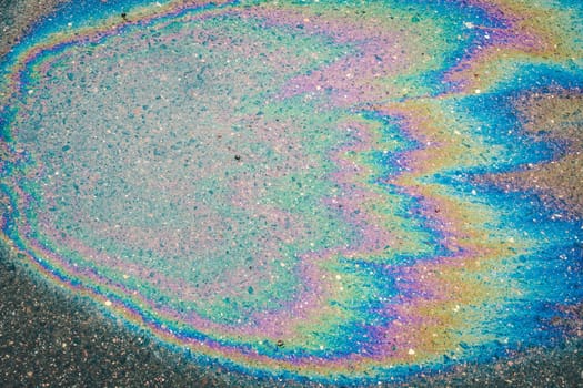 Iridescent multi-colored stain from engine oil on asphalt close-up