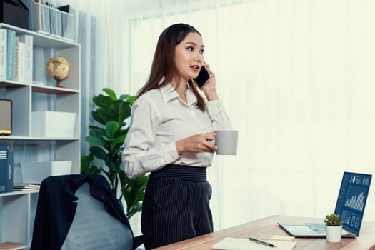 Young enthusiastic businesswoman talking on business call and writing notes on her laptop as multitask office lady. Female employee writing business tasks while talking on phone call with clients.