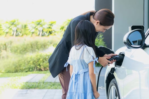 Progressive lifestyle of mother and daughter who have just returned from school in an electric vehicle that is being charged at home. Electric vehicle powered by sustainable clean energy.