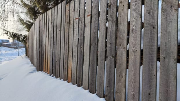 Fence made of wooden slats and snow on a winter day. Location, Background, texture, copy of space, frame as graphic resource