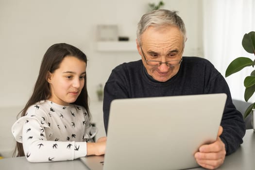 Portrait of senior man and young girl granddaughter using laptop at home