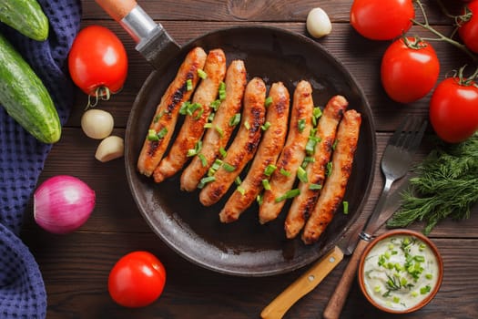 Delicious sausages cooked in a pan with vegetables and various sauces on a wooden table.