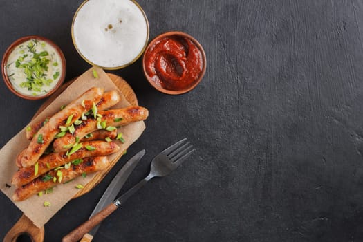 Tasty sausages on a wooden board with various sauces with a glass of beer on a black background. copy space.