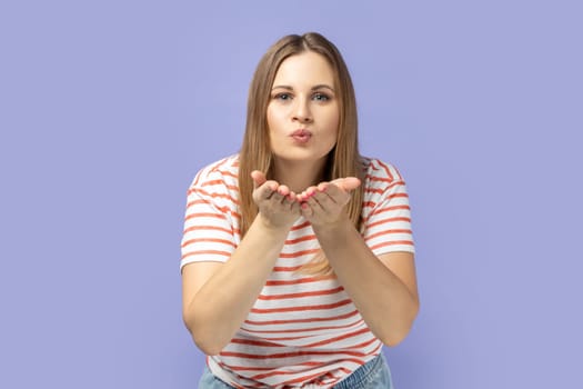 Portrait of lovely beautiful woman sending air kiss looking at camera, flirting and demonstrating love affection feelings, romantic relationships. Indoor studio shot isolated on purple background.