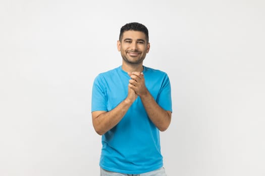 Portrait of positive optimistic smiling unshaven man wearing blue T- shirt standing applauding, being satisfied of performance, enjoying. Indoor studio shot isolated on gray background.