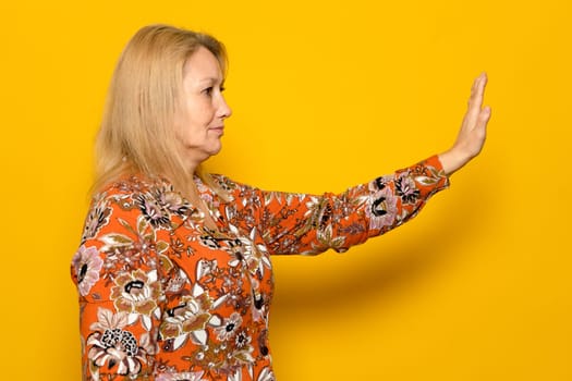 No, forbidden. Side view of upset attractive woman in patterned dress showing stop gesture, prohibition or warning expression. Indoor studio shot isolated on yellow background.