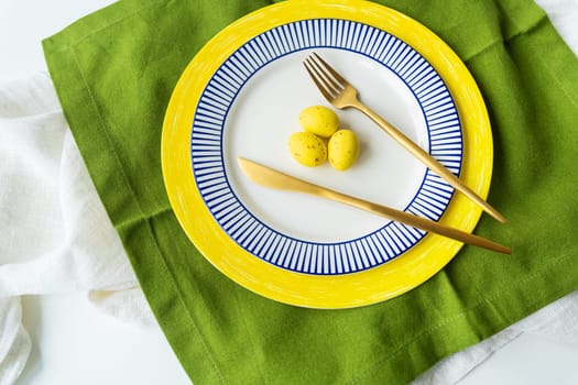 Easter serving concept. Festive table setting with bright napkins and yellow-blue plates with dishes and decorated eggs