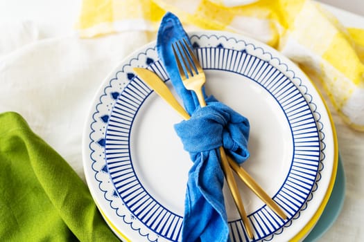 Serving design. Easter serving concept. Gold cutlery is tied with a blue napkin, on which the plates are on a green-yellow linen napkin. Minimalistic design