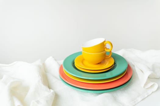 Empty yellow cups and brightly colored plates on a white table covered with a linen tablecloth