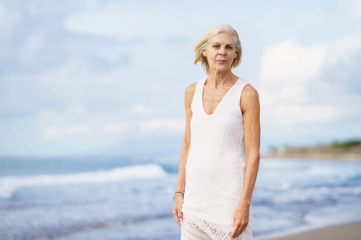 Portrait of smiling mature woman walking on the beach. Elderly female enjoying her retirement at a seaside location.