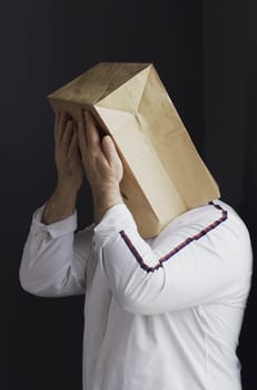 A sad man in a white shirt with a bag on his head, with a drawn crying emoticon, stands against the wall and cries. Emotions and gestures. Vertical frame.