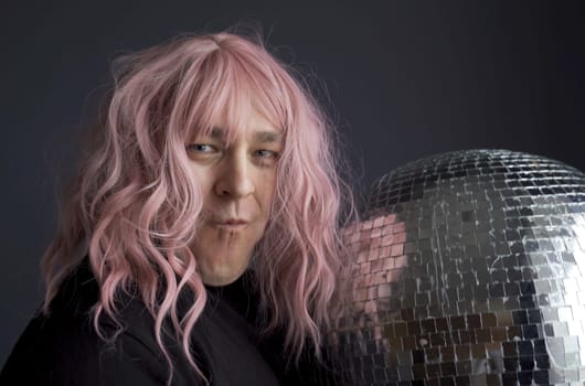 Portrait of a man in a pink wig holding a disco ball. Close-up.