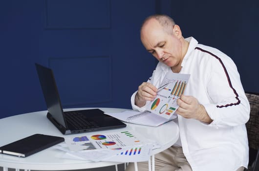 A man makes an online video call chat, sitting at home and talking into a laptop webcam, showing a document.