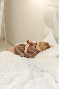 Portrait of a boy in a brown bathrobe, who is lying in bed, resting.