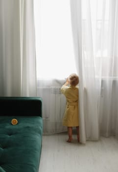 A little boy in a dressing gown stands near the window and looks.