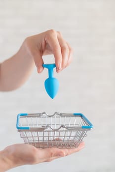 Faceless gynecologist puts anal plug in miniature shopping baskets. The doctor holds the device for alternative sex. A practitioner recommends a silicone toy for safety