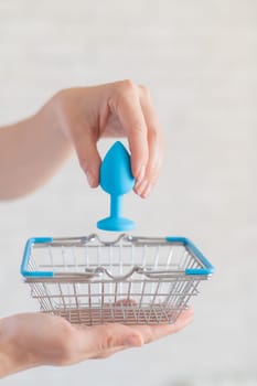 Faceless gynecologist puts anal plug in miniature shopping baskets. The doctor holds the device for alternative sex. A practitioner recommends a silicone toy for safety