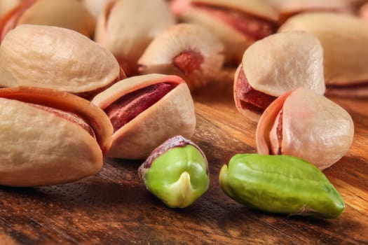 Pile of red Turkish pistachios on wooden board. Two of them peeled, green nut visible.