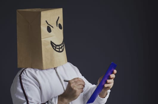 An angry man in a white shirt with a bag on his head, with a drawn angry smiley face, holds a tablet in his hands and crosses out from the list of candidates for the award.