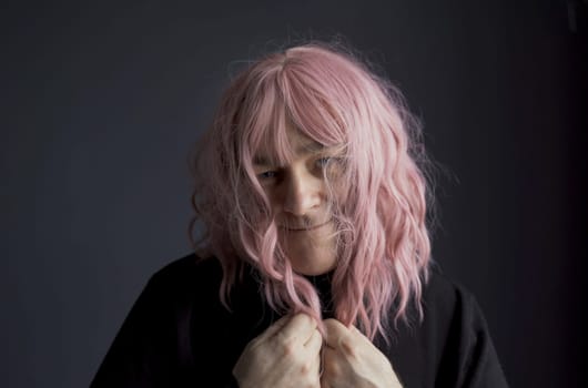 Portrait of a man who tried on a pink wig, looks at the camera, grimaces, poses. Close-up.