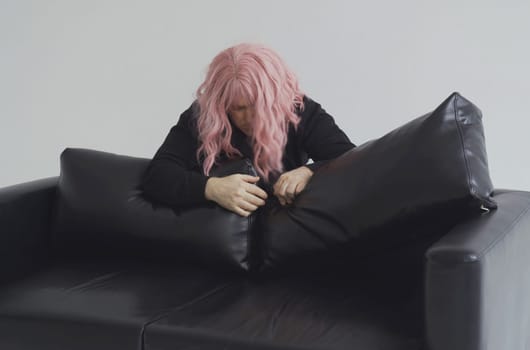 A drunken man in a pink wig climbs over the sofa and falls asleep.