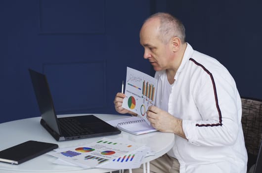 A man makes an online video call chat, sitting at home and talking into a laptop webcam, showing a document.