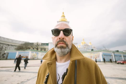 Attractive fashionable man with beard in stylish brown coat in city street in Kyiv