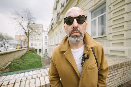 Attractive fashionable man with beard in stylish brown coat in city street in Kyiv