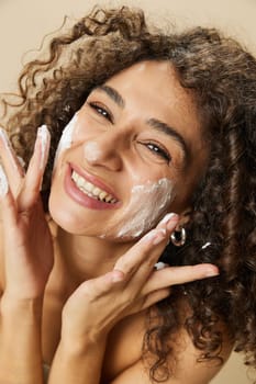 Woman beauty face close-up applying foam to wash and cleanse skin with fingers of her hand, nail and hair health, hair dryer style curly afro hair, body and beauty care concept. High quality photo