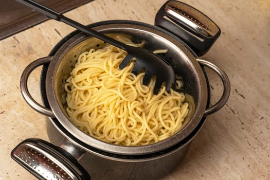 we cook ourselves. boiled ready-made spaghetti in a colander and a kitchen saucepan. pot with spaghetti and skimmer. cooking spaghetti. homemade Italian-style dinner. Pasta cooking. close-up