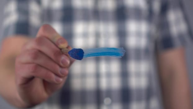 A young man draws a mathematical minus sign on the glass. A man in a shirt draws with a brush and blue paint. Close-up. 4k