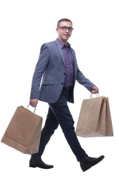 Young businessman wearing jeans and glasses with shopping bags walking against a white background.