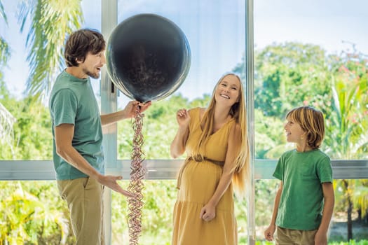 Expectant parents mother, father and their elder son are having a gender reveal party. A married couple holds a black balloon with the inscription Boy and Girl.Family, pregnancy and prenatal care concept.