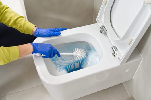 Wall mounted toilet cleaning with detergent. Woman hotel maid cleans a bathroom toilet with a scrub brush. household service. Modern flush toilet. Cleaning