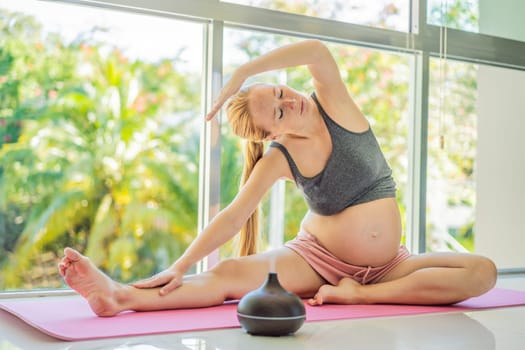 Young pregnant woman doing yoga exercises and meditating at home with an aroma diffuser. Health care, mindfulness, relaxation and wellness concept. Aromatherapy during pregnancy.