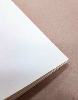 A corner of a stack of white paper sheets lies on a brown background. Space for text. Top view, vertical.
