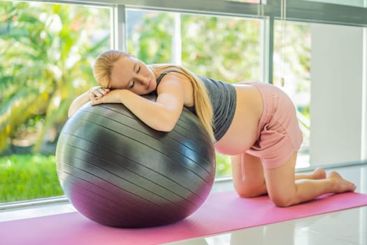 Pregnant woman exercising on fitball at home. Pregnant woman doing relax exercises with a fitness pilates ball. Against the background of the window.