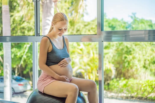 Pregnant woman exercising on fitball at home. Pregnant woman doing relax exercises with a fitness pilates ball. Against the background of the window.