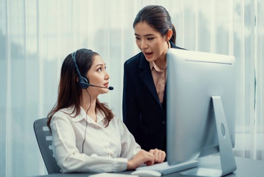 Asian female customer support operator wearing headset is guided by her supportive manager. Experienced colleague help operator handle a call with a client, providing advice and guidance. Enthusiastic