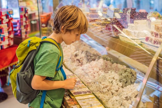 The boy looks at the counter with Turkish sweets. Traditional oriental sweet pastry cookies, nuts, dried fruits, pastilles, marmalade, Turkish desert with sugar, honey and pistachio, in display at a street food market.