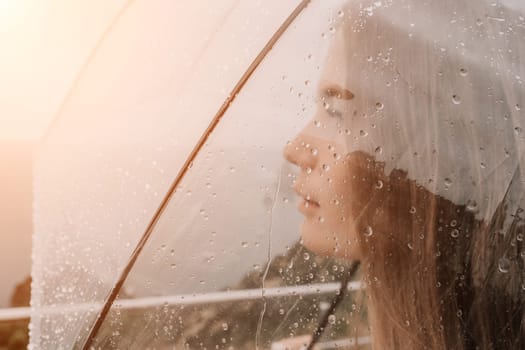 Woman rain park. Happy woman portrait wearing a raincoat with transparent umbrella outdoors on rainy day in park near sea. Girl on the nature on rainy overcast day