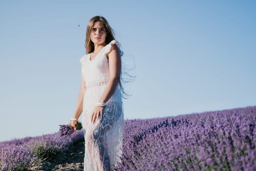 Close up portrait of young beautiful woman in a white dress and a hat is walking in the lavender field and smelling lavender bouquet.