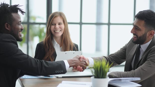 Sealing a deal. Business people shaking hands while sitting at the desk in office