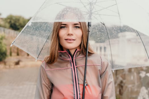 Woman rain park. Happy woman portrait wearing a raincoat with transparent umbrella outdoors on rainy day in park near sea. Girl on the nature on rainy overcast day