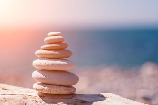 Balanced Pebbles Pyramid on the Beach on Sunny Day and Clear Sky at Sunset. Blue Sea on Background Selective focus, zen stones on sea beach, meditation, spa, harmony, calm, balance concept.