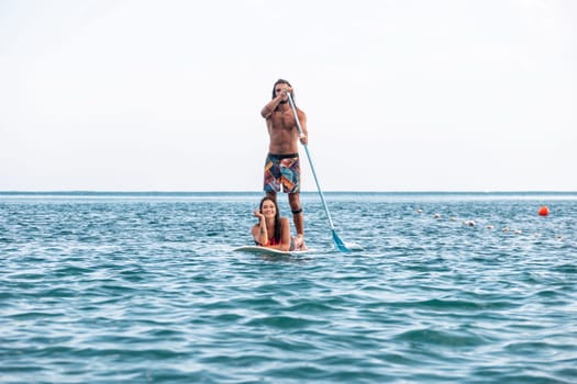 Sea woman and man on sup. Silhouette of happy young woman and man, surfing on SUP board, confident paddling through water surface. Idyllic sunset. Active lifestyle at sea or river