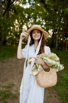 a happy woman in a light summer dress stands in nature with a wicker hat, a plaid and a basket with daisies. High quality photo