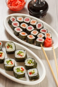 Different sushi rolls with rice and seaweed sheets on ceramic plates, chopsticks, glass bottle with soy sauce and pickled ginger in a bowl. Top view.