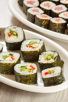 Different sushi rolls with rice and seaweed sheets on ceramic plates. Top view.